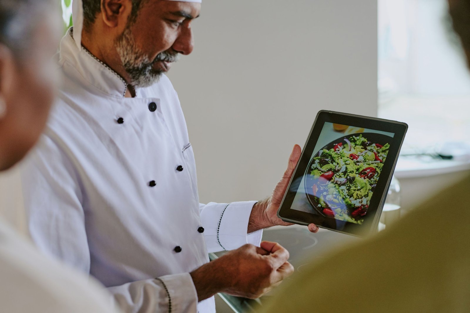 High angle shot of Indian chef demonstrating salad with baked tomatoes and pesto sauce to his unrecognizable cooks