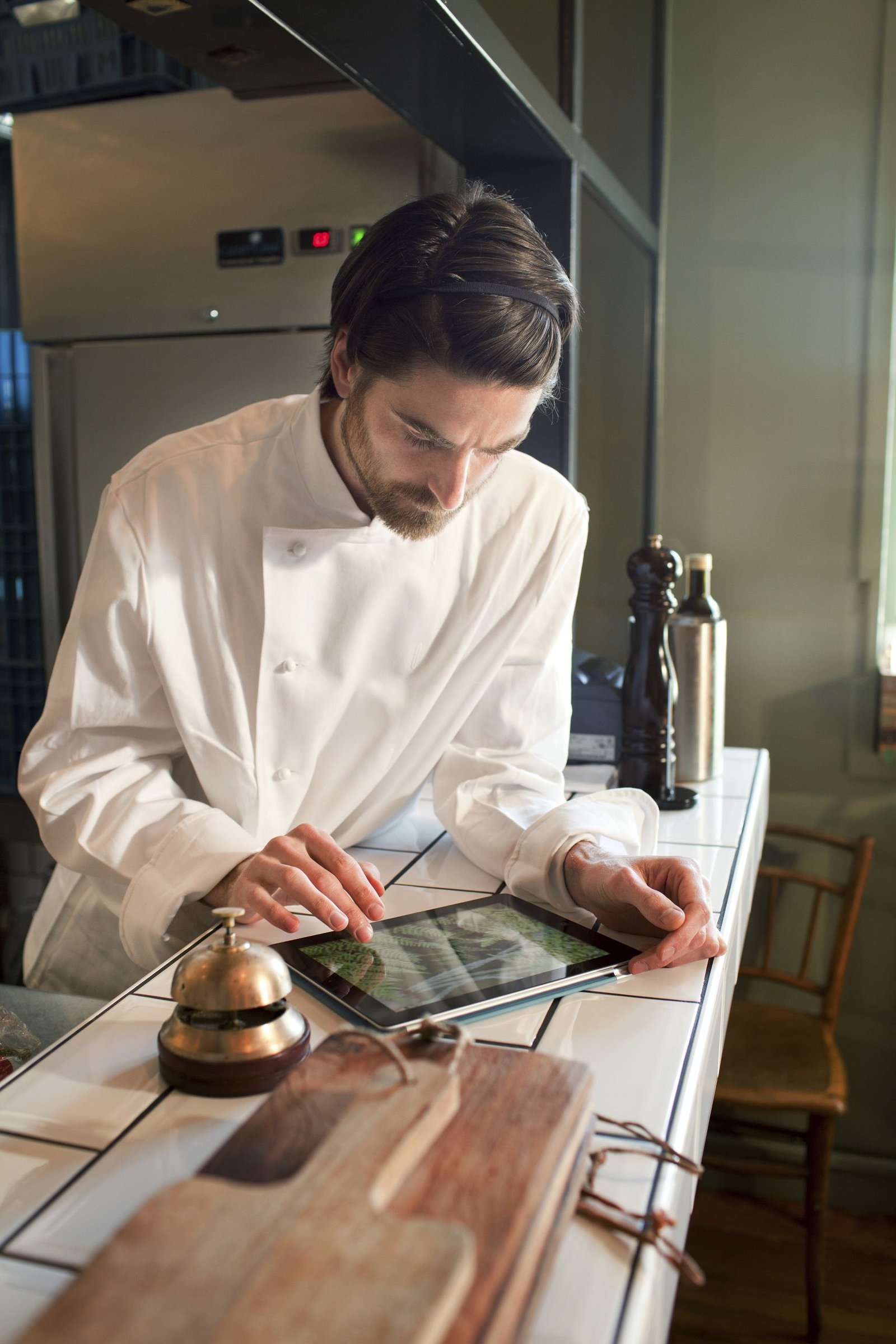 Chef elegantly inspecting a recipe on a digital tablet in a professional kitchen